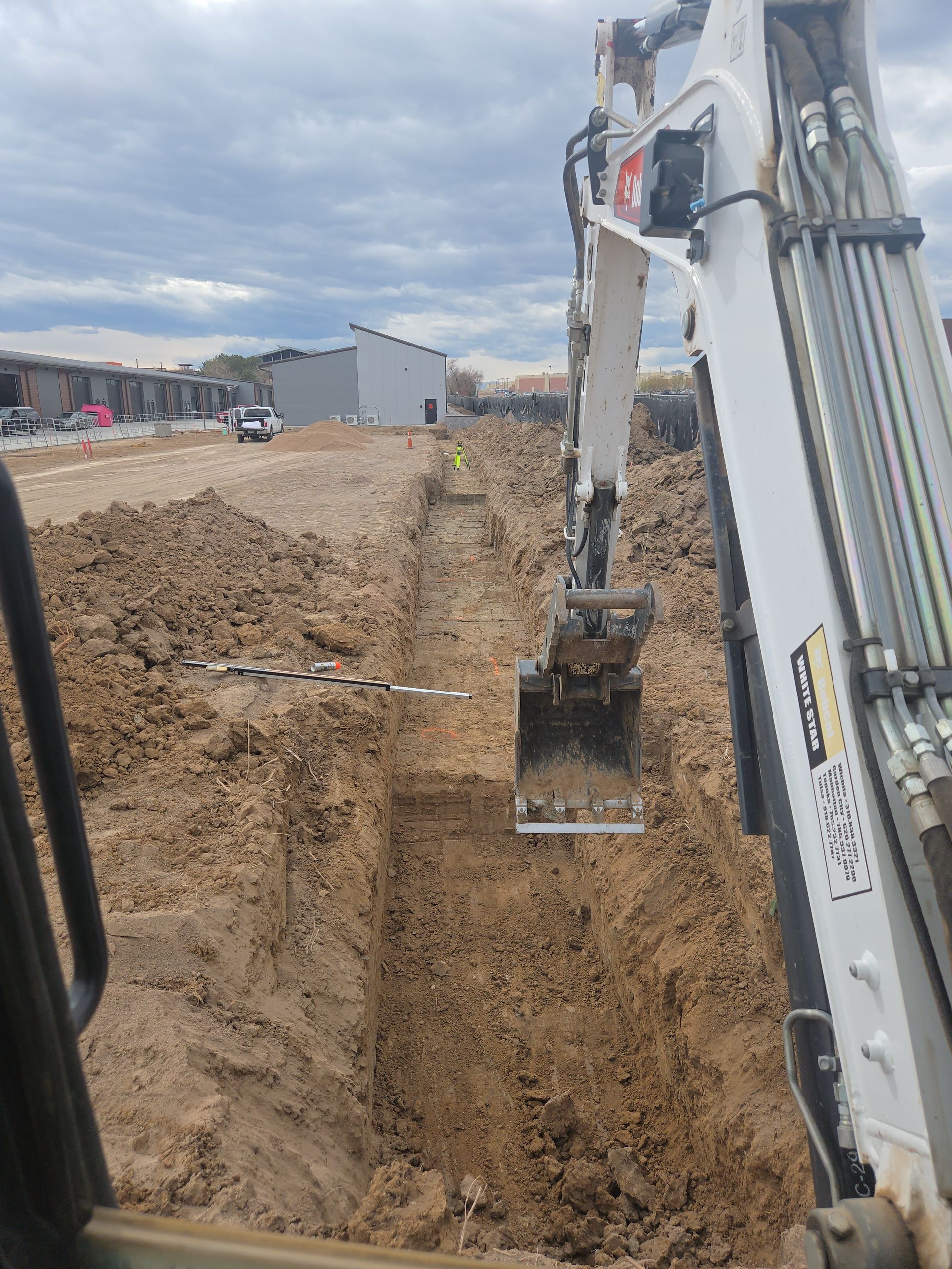 Excavator digging a deep trench at a construction site on a cloudy day