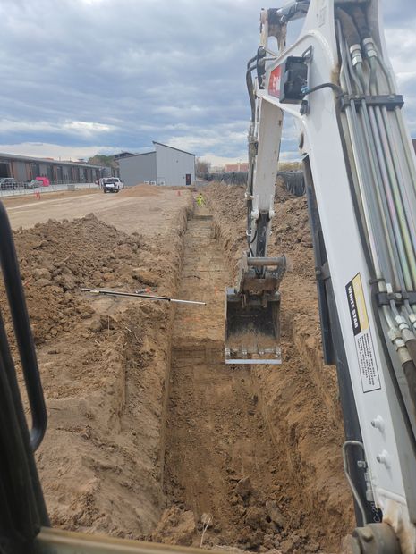 Excavator digging a deep trench at a construction site on a cloudy day
