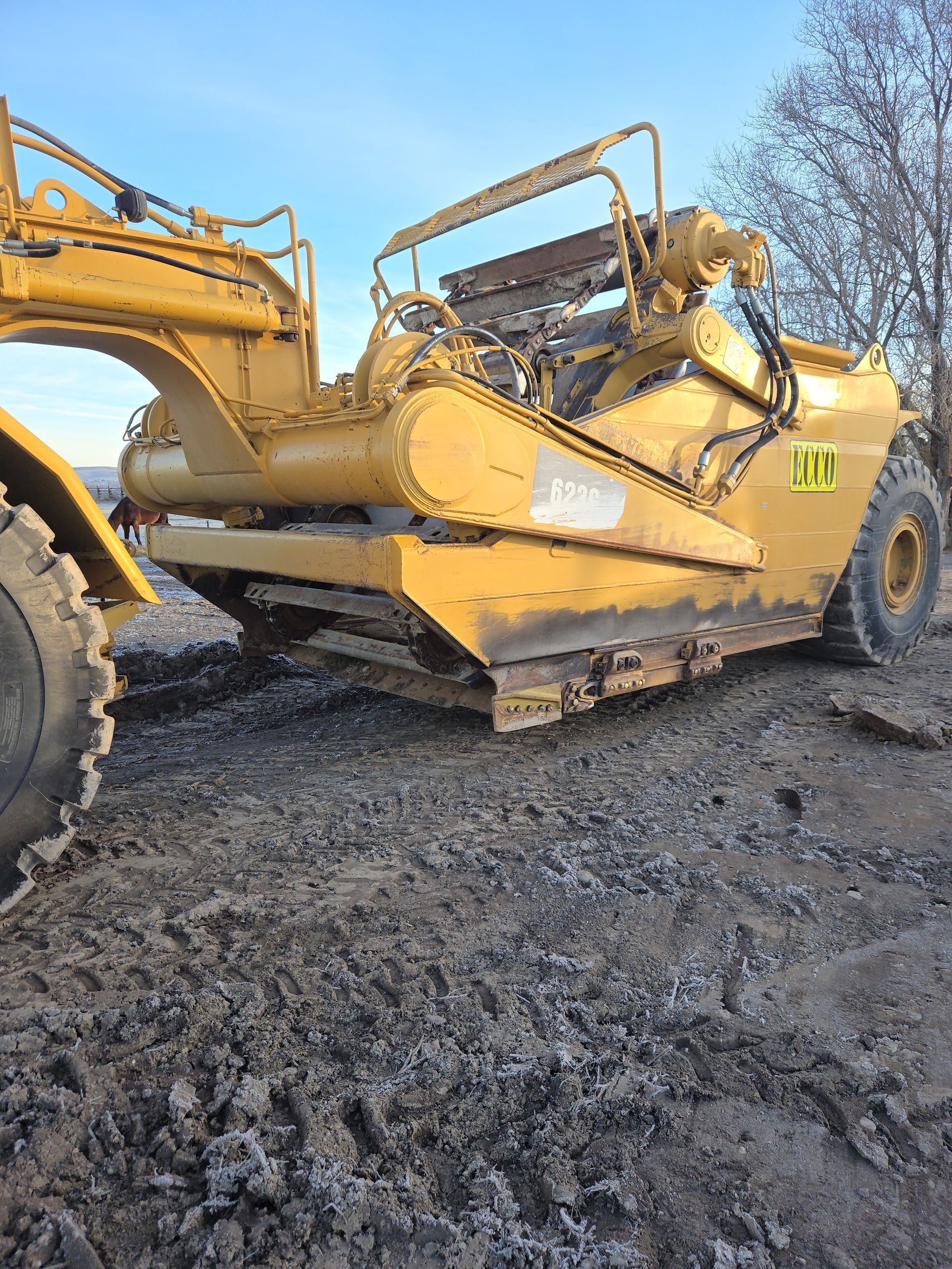 Yellow construction vehicle on muddy ground, with debris piled in its open hopper.
