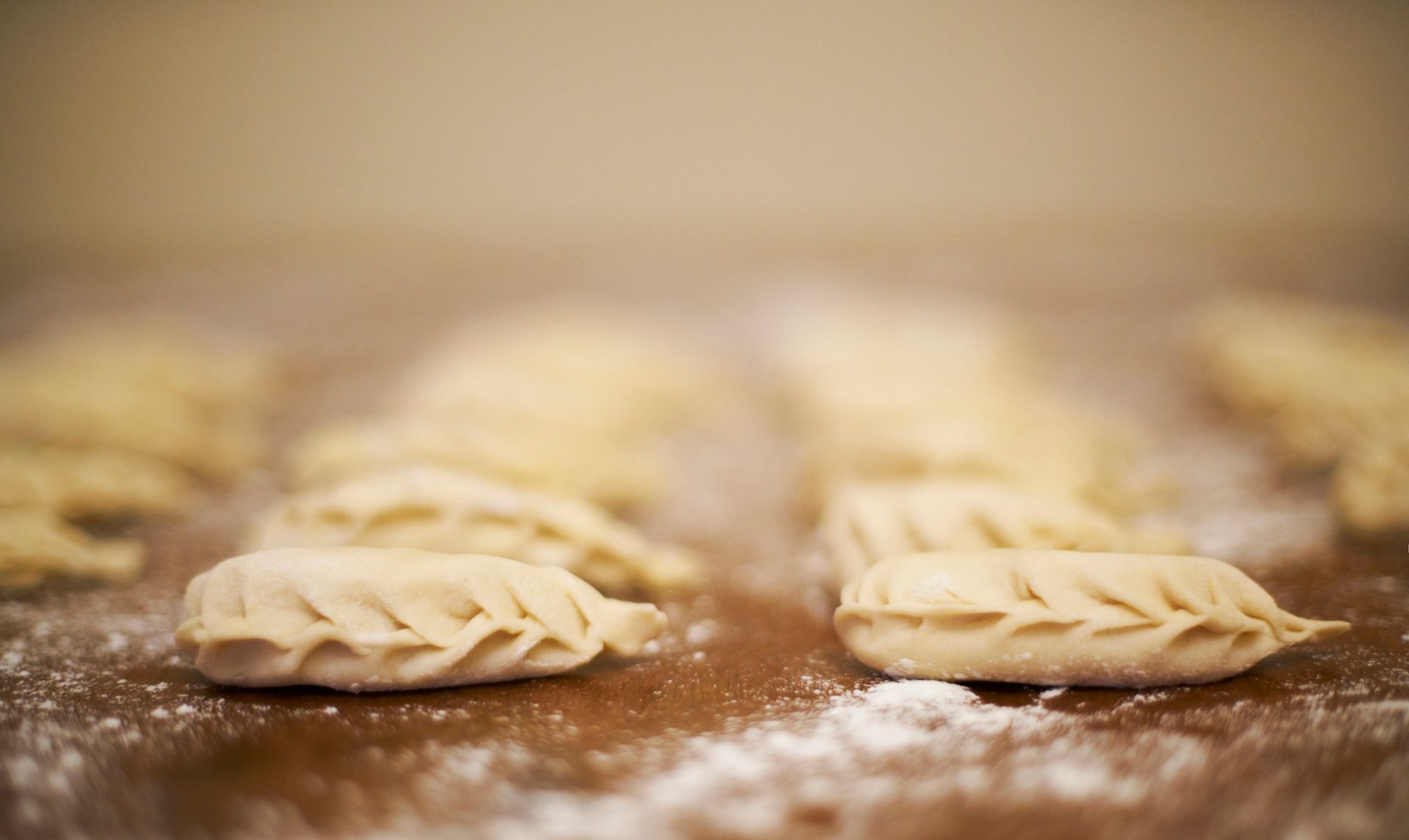 Primo piano di pierogi crudi su una superficie di legno spolverata di farina.