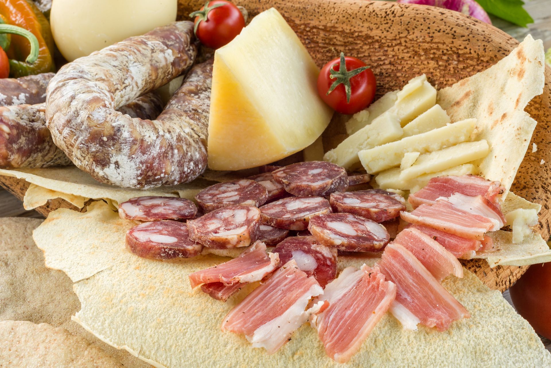 Assortimento di salumi, formaggi e pomodori su un pane simile a un cracker; primo piano.