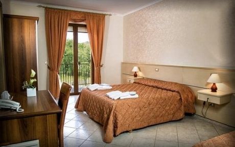 Una luminosa camera d'albergo dotata di un letto con copriletto trapuntato color cuoio, una scrivania in legno