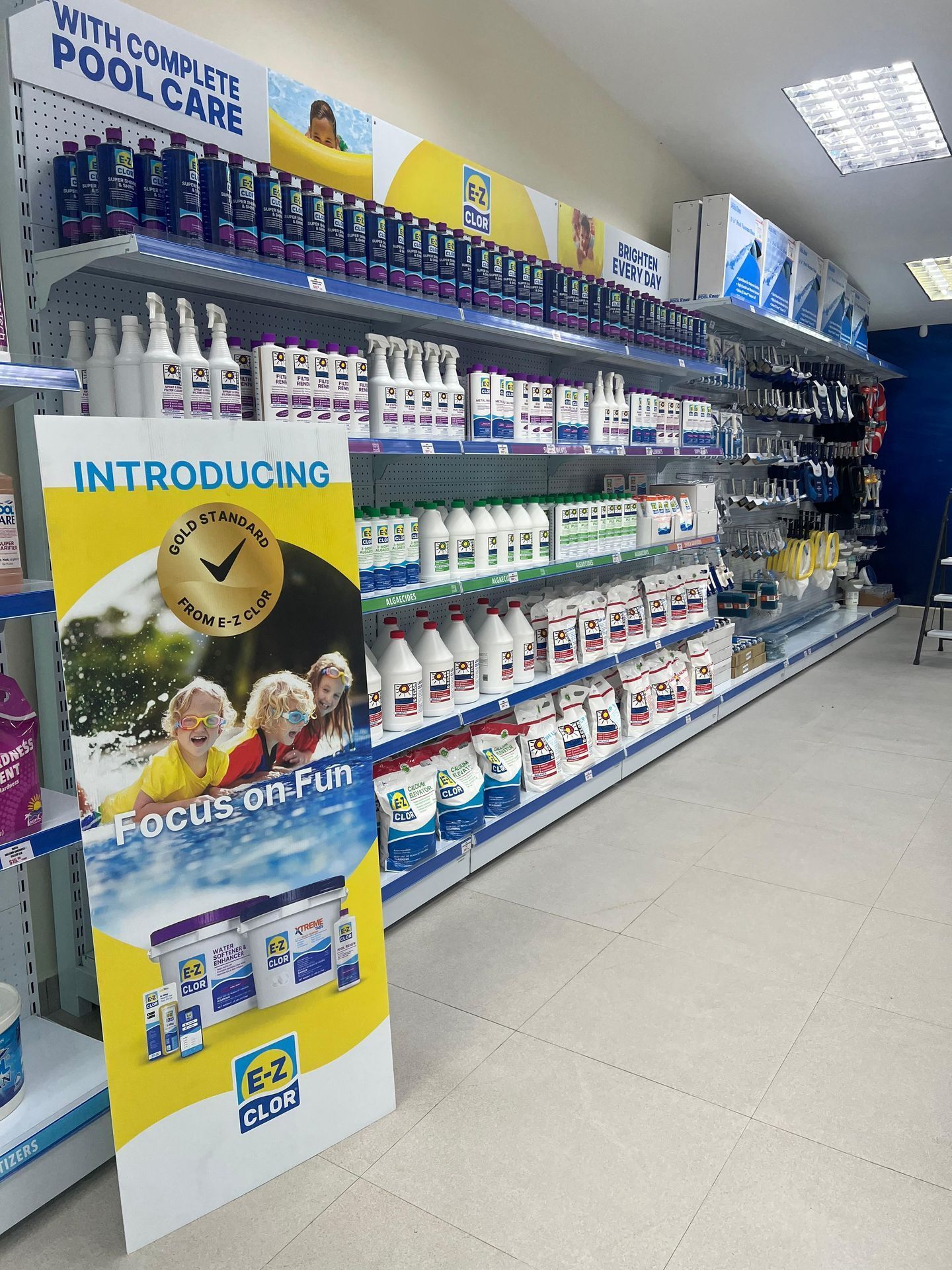 Pasillo de productos para el cuidado de piscinas en una tienda, con estantes llenos de productos de limpieza y un cartel amarillo que indica el producto.