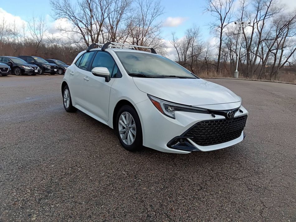 White sedan parked on a gravel lot with bare trees in the background