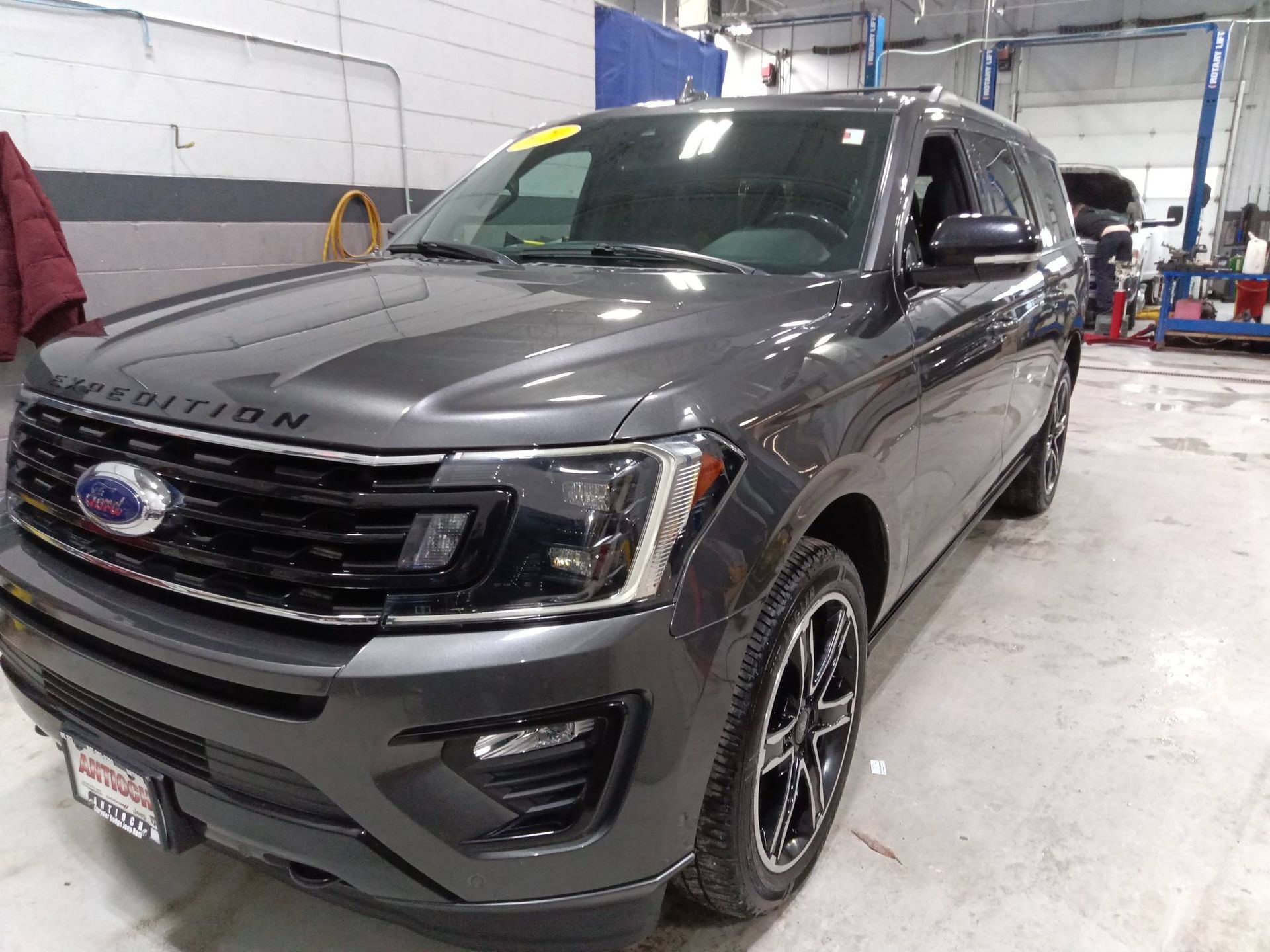 Gray Ford Expedition SUV in an auto shop, front-left view, with raised hood and service bay background