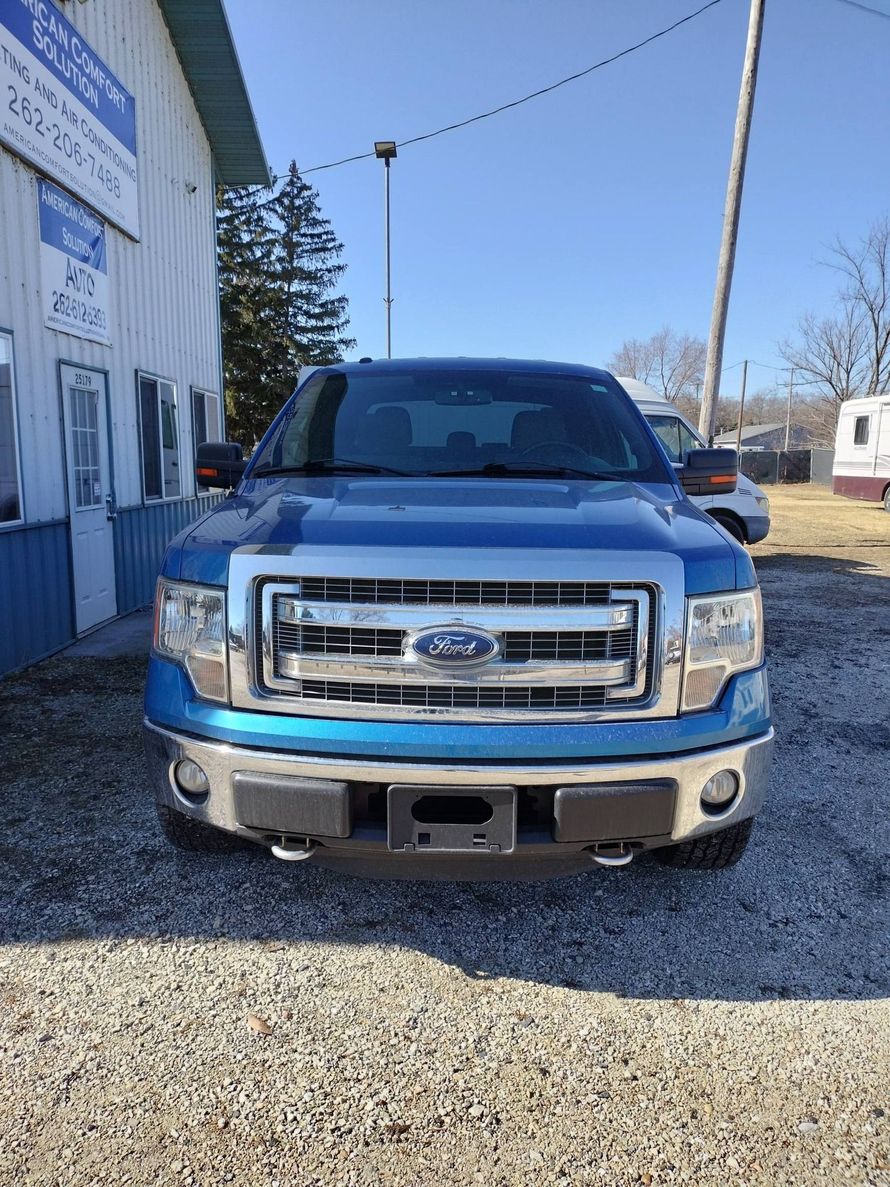 Blue Ford pickup truck parked on gravel outside a building on a sunny day