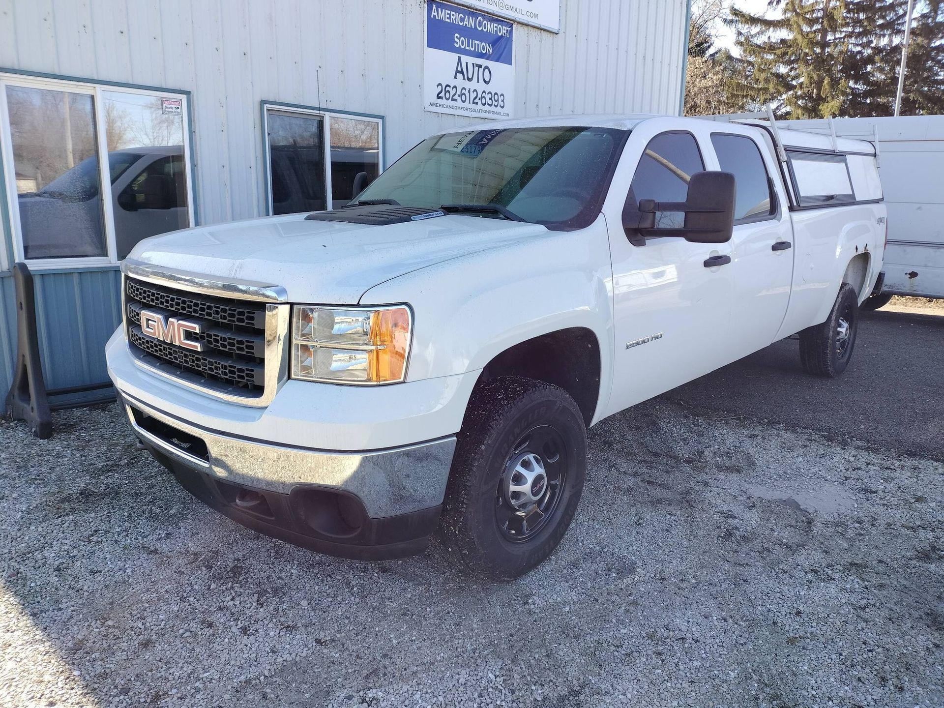 White GMC pickup truck parked outside a building on gravel.