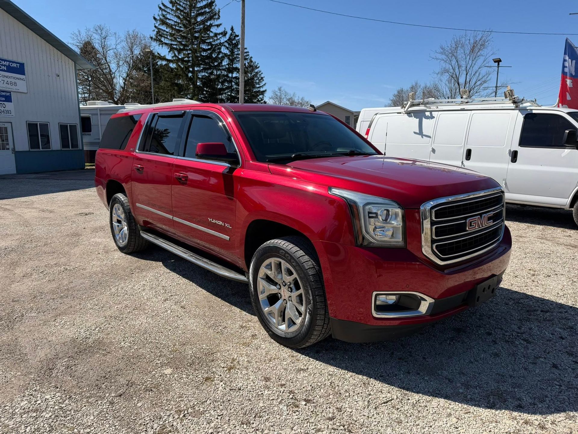 Red GMC SUV parked on a gravel lot beside white vans under a clear blue sky