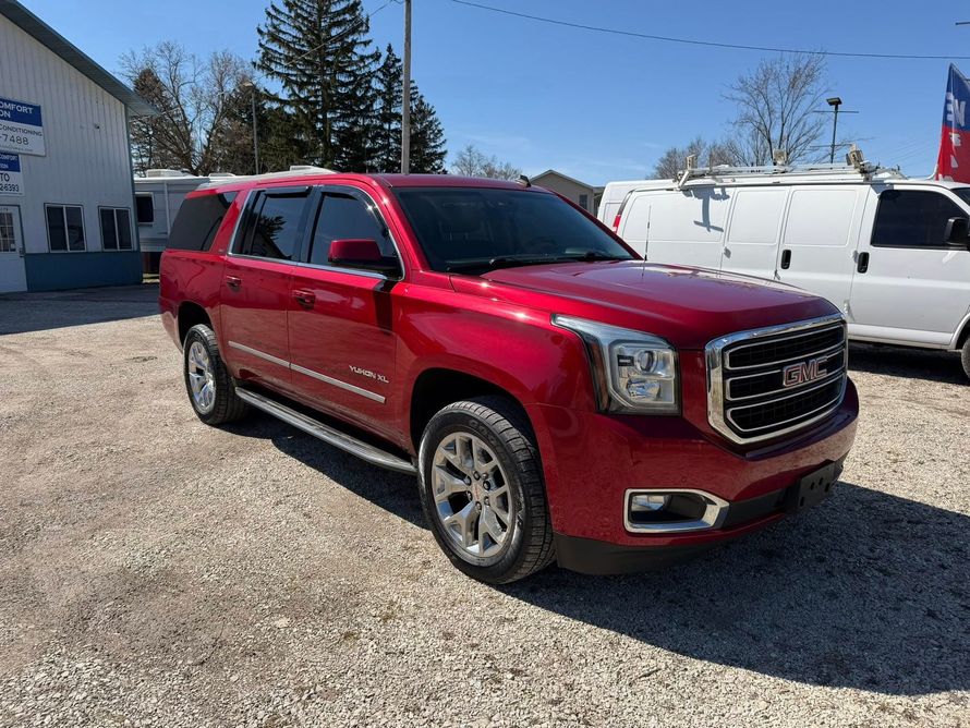 Red SUV parked on a gravel lot beside white vans under a clear blue sky