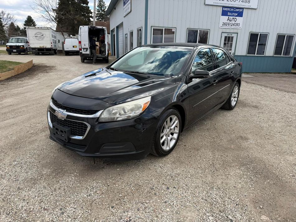 Black sedan parked on a gravel lot beside a building and tow trucks