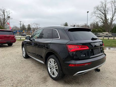 Black SUV parked on a gravel lot under a cloudy sky, seen from the rear side