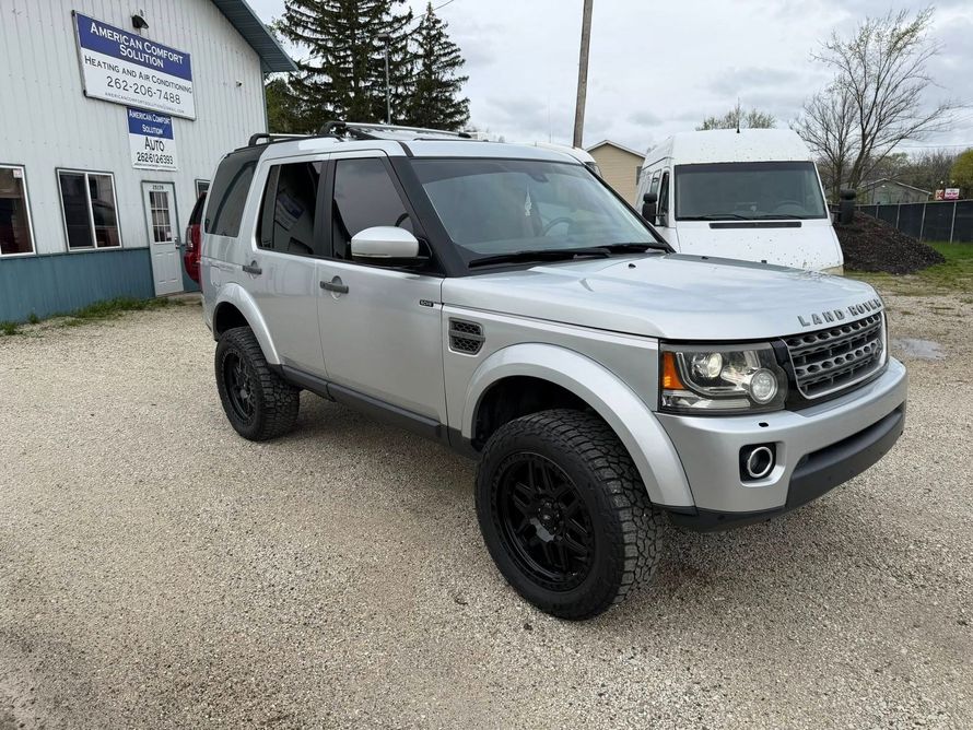 Silver Land Rover SUV parked outside a building on a gravel lot, with a white van in the background