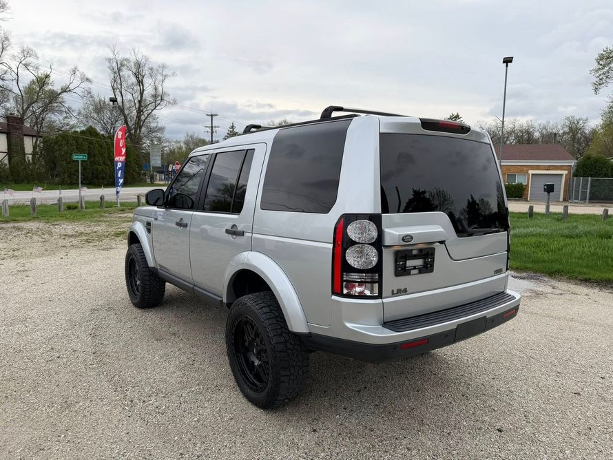 Silver SUV parked on gravel near a road, viewed from the rear-left side.