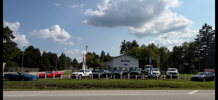 Used car lot with parked trucks and SUVs beside a red-and-blue feather flag outdoors