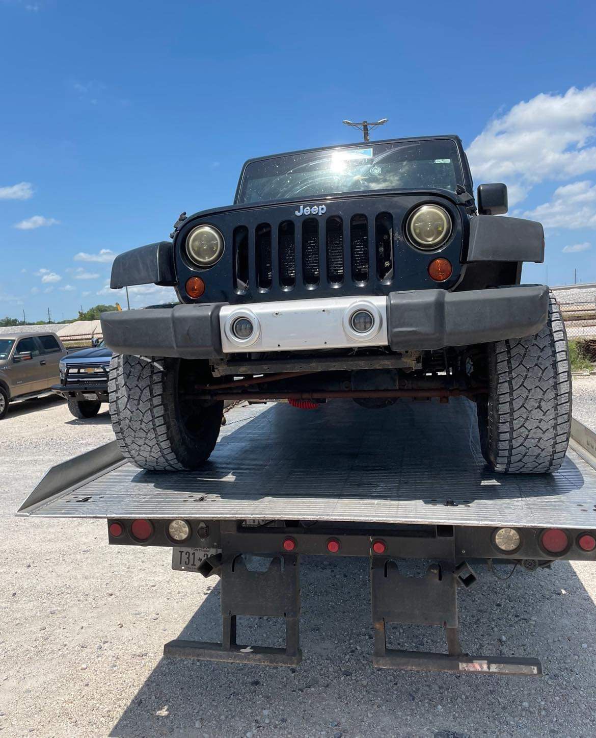Black Jeep Wrangler on a flatbed tow truck under a blue sky
