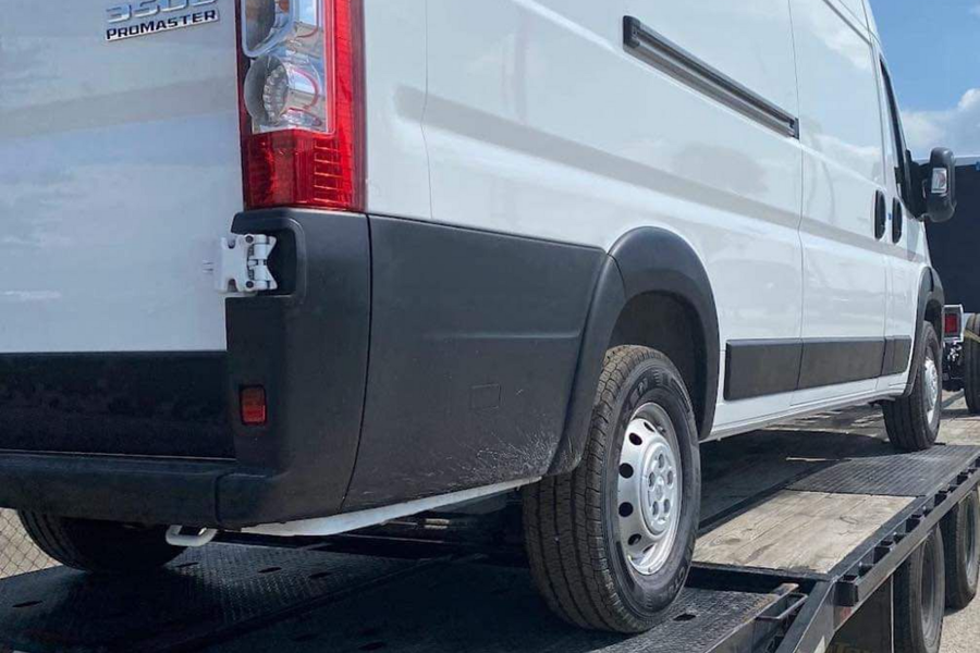 White cargo van on a tow truck bed, rear side view.