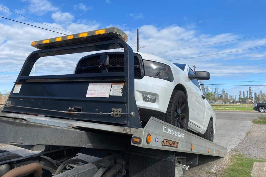 White car on a tow truck ramp under a blue sky.