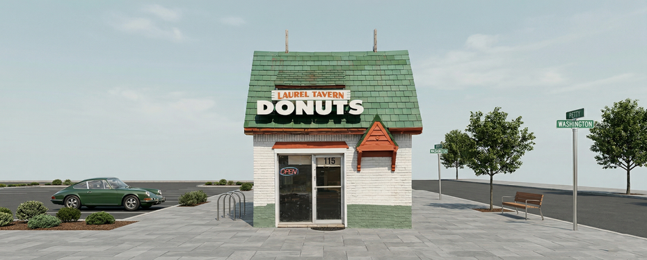A small, white and green donut shop with a green roof, standing beside a parking lot and a street sign on a sunny day.