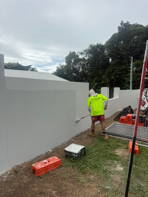 Worker in yellow jacket painting the exterior of a blue building from a suspended bucket lift