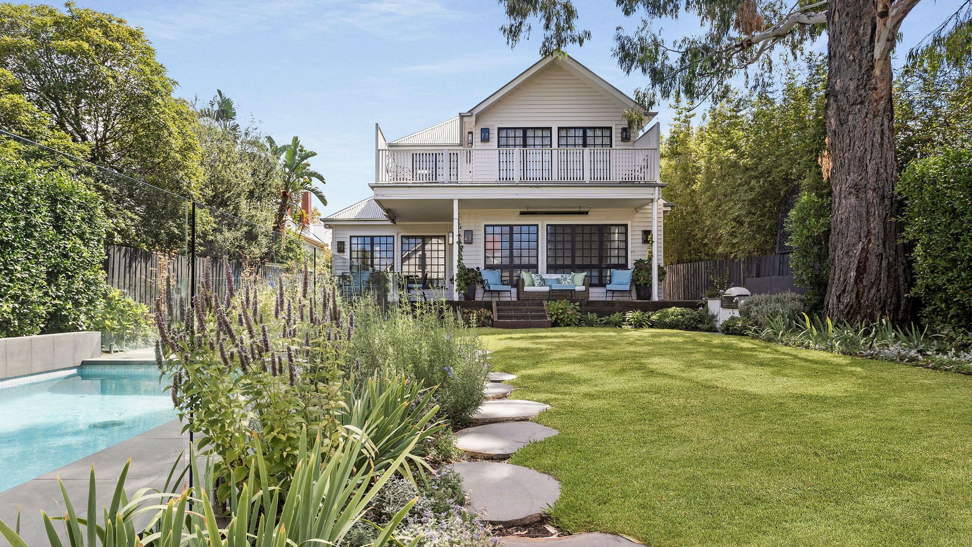 Two-story house with balcony, pool, and pathway through green lawn.