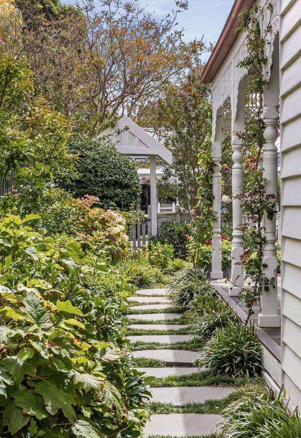 Stone path through lush garden leads to a white gazebo; white house with porch on right.