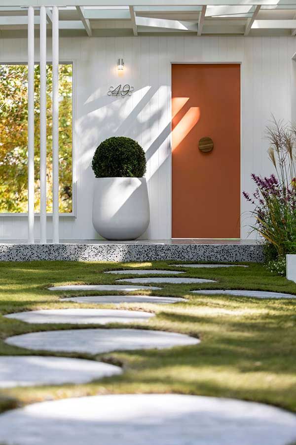Exterior view of a white building with an orange door and a pathway of stepping stones through the grass.