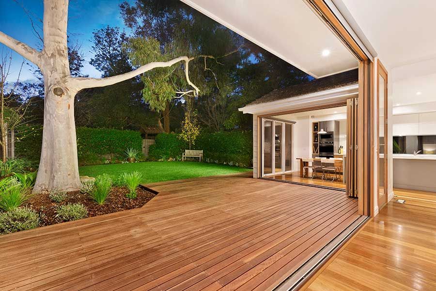 Wooden deck opens to a backyard with a large tree. Interior view of kitchen and dining area.