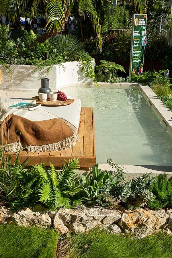 Outdoor dining setting beside a pool, surrounded by lush greenery and stone accents.