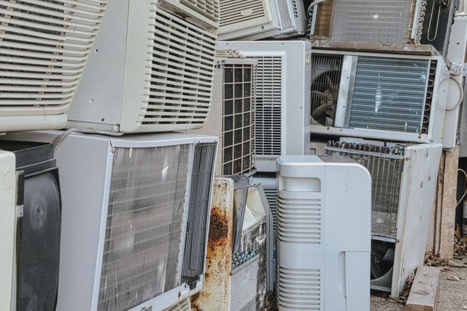 Piled old air conditioners and metal units stacked outdoors, showing rust and grime