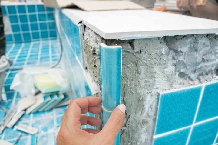 Hand tiling pool edge with teal ceramic tiles and cement.