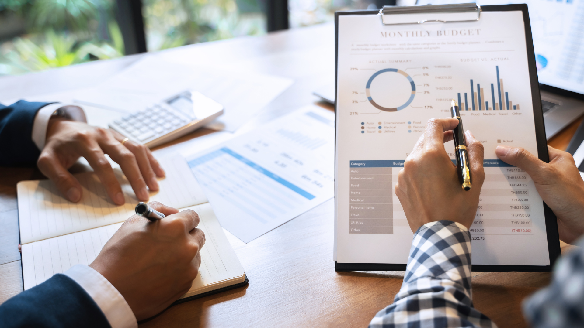 two people are sitting at a table looking at a clipboard with a graph on it .