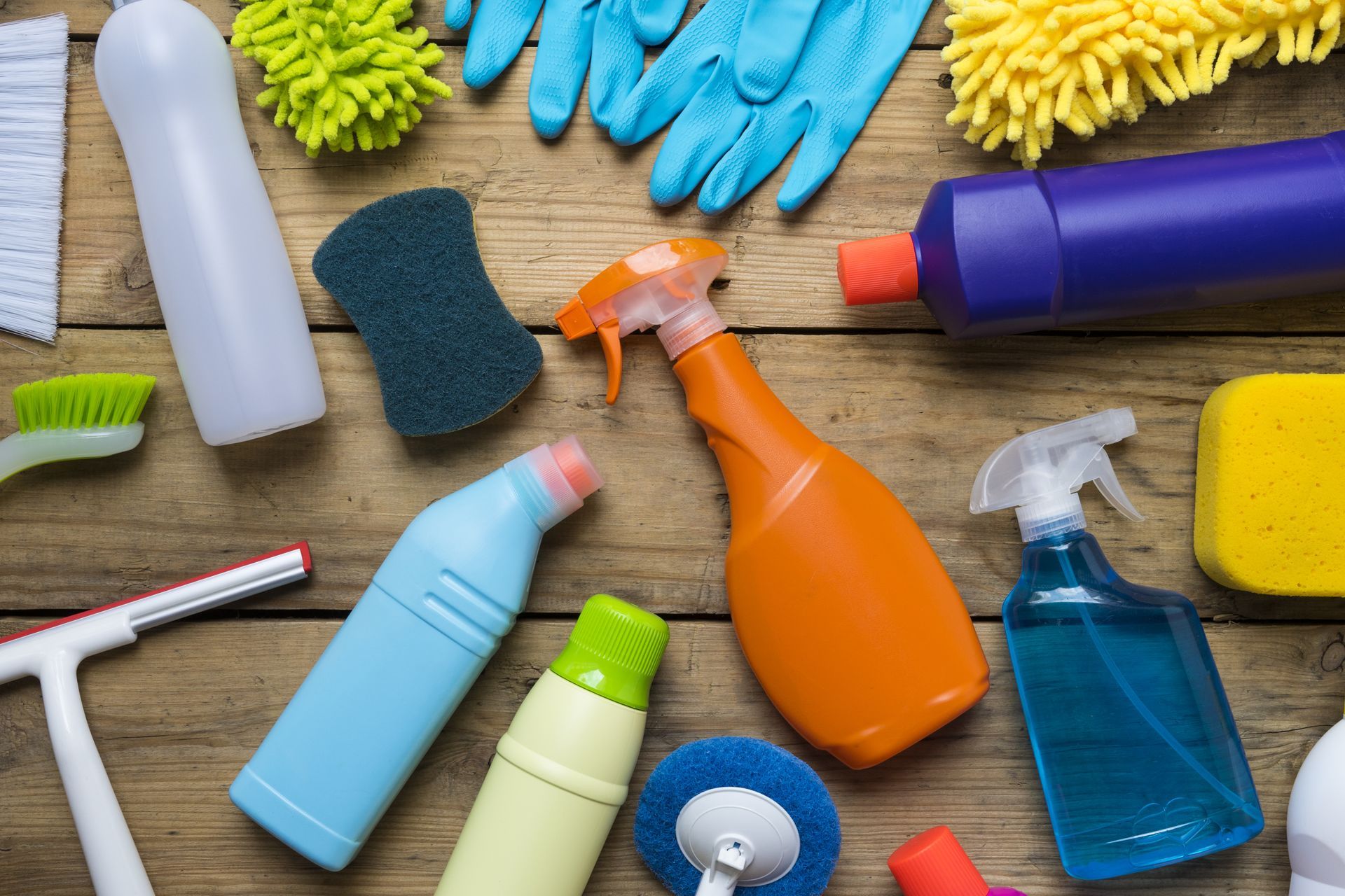 Assorted colorful cleaning supplies and tools arranged on a wooden surface.