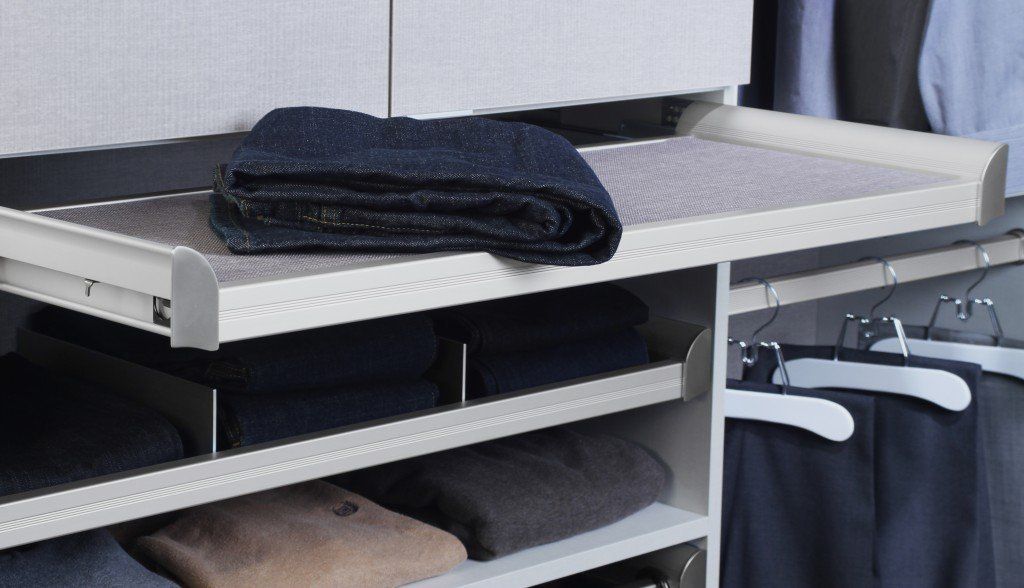 Folded dark towel on a white shelf above hanging clothes in a closet.