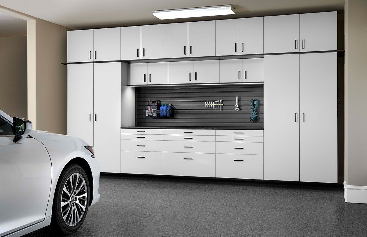 A car is parked in a garage with white cabinets.