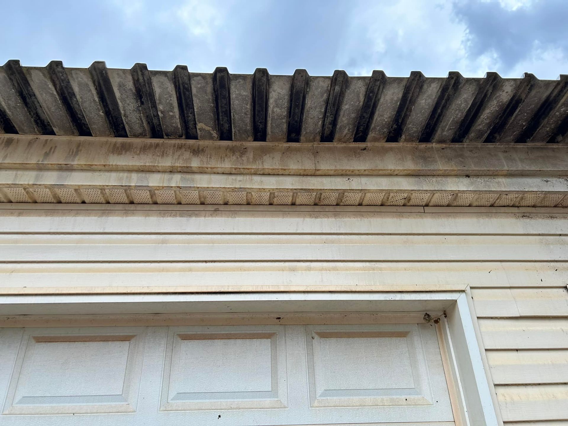 Close-up of a white house roofline with weathered corrugated eaves against a cloudy sky
