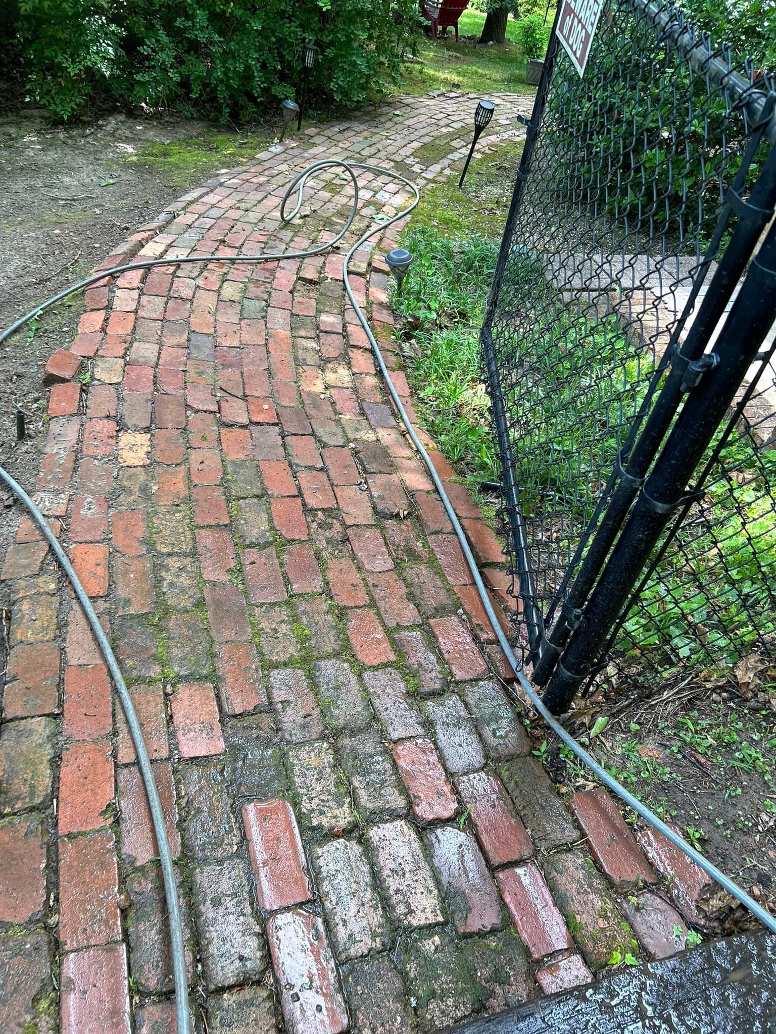 Curving brick garden path beside a black metal gate and green plants