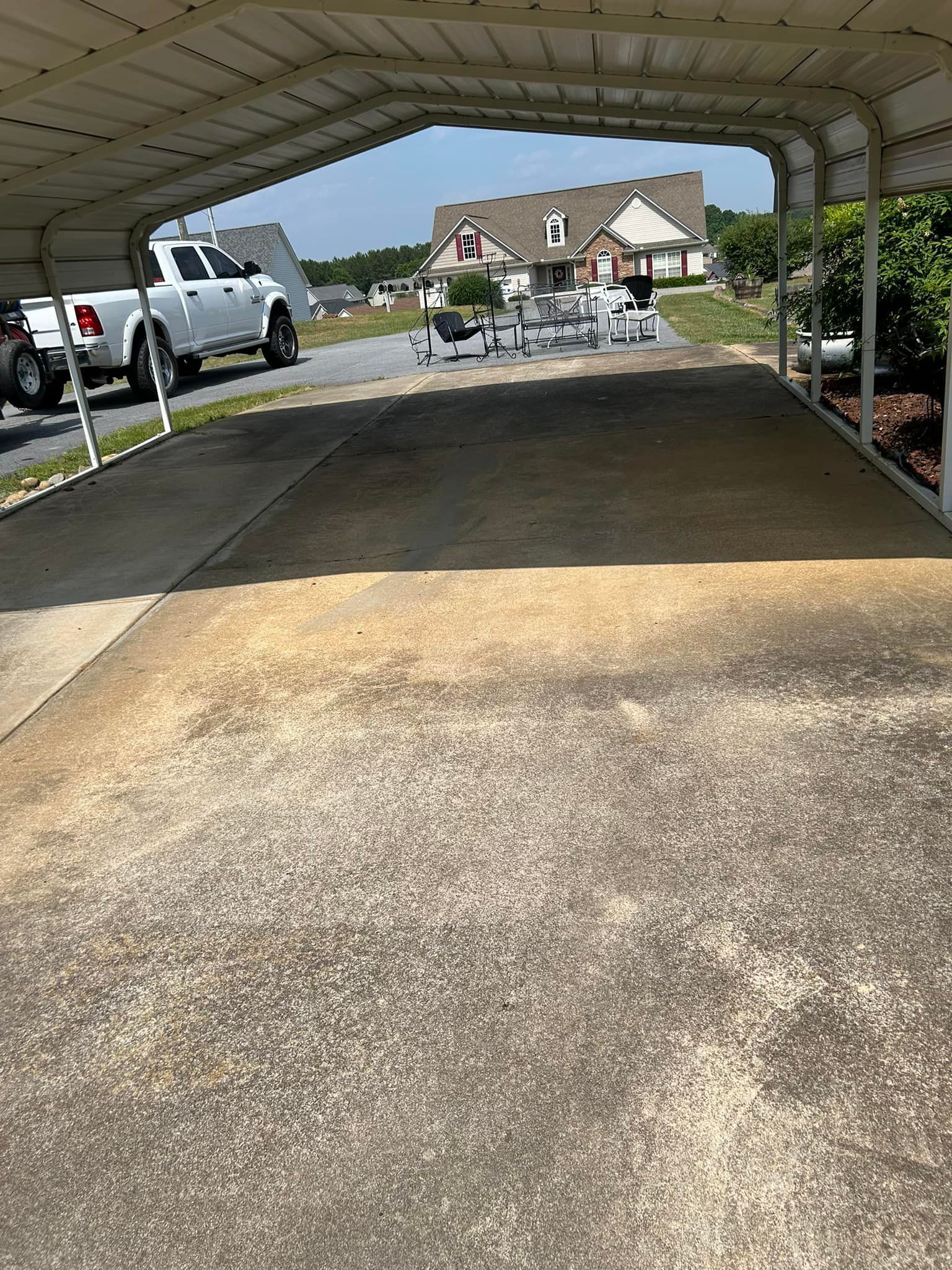 Carport with a concrete driveway leading to a suburban house on a sunny day. A white truck is parked.