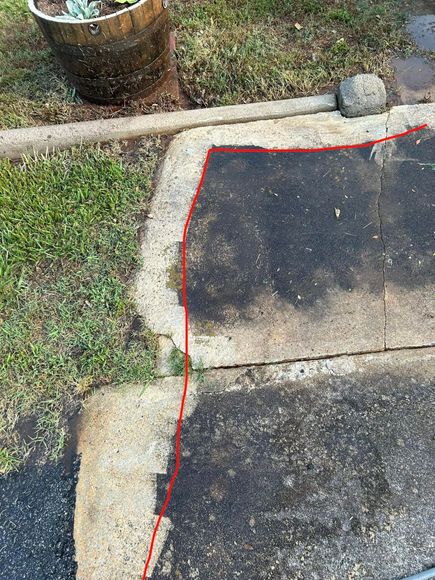 Concrete walkway with a red line indicating a barrier, next to grass and a wooden planter.