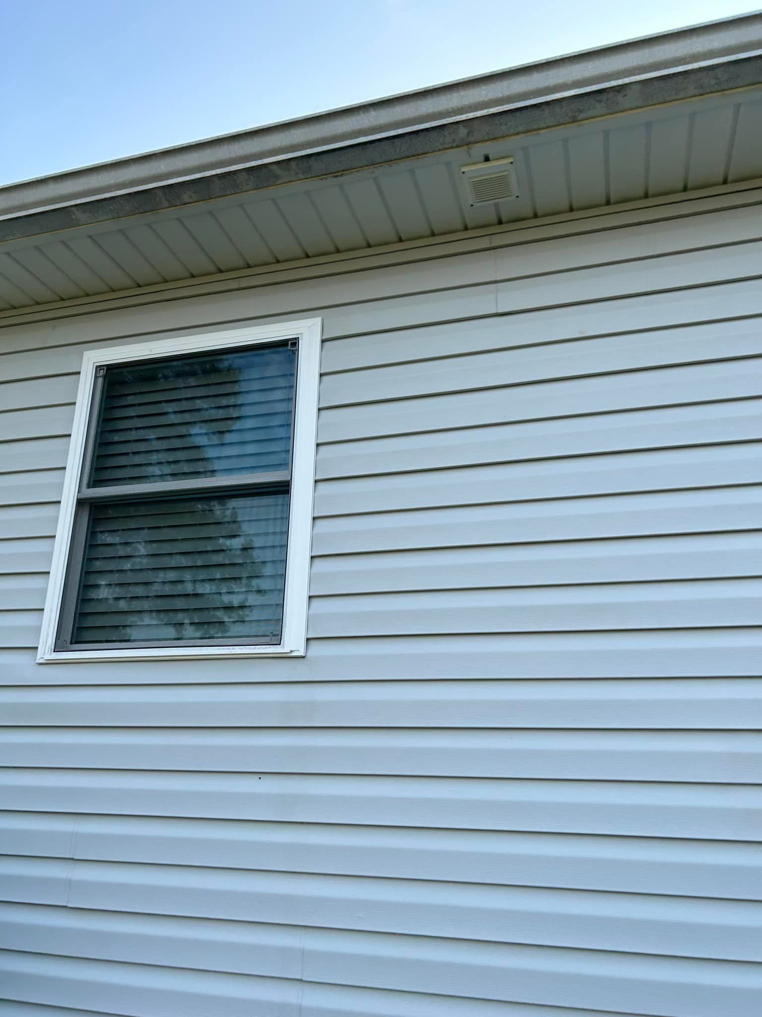 Side of a house with light gray vinyl siding and a white-framed window with closed blinds