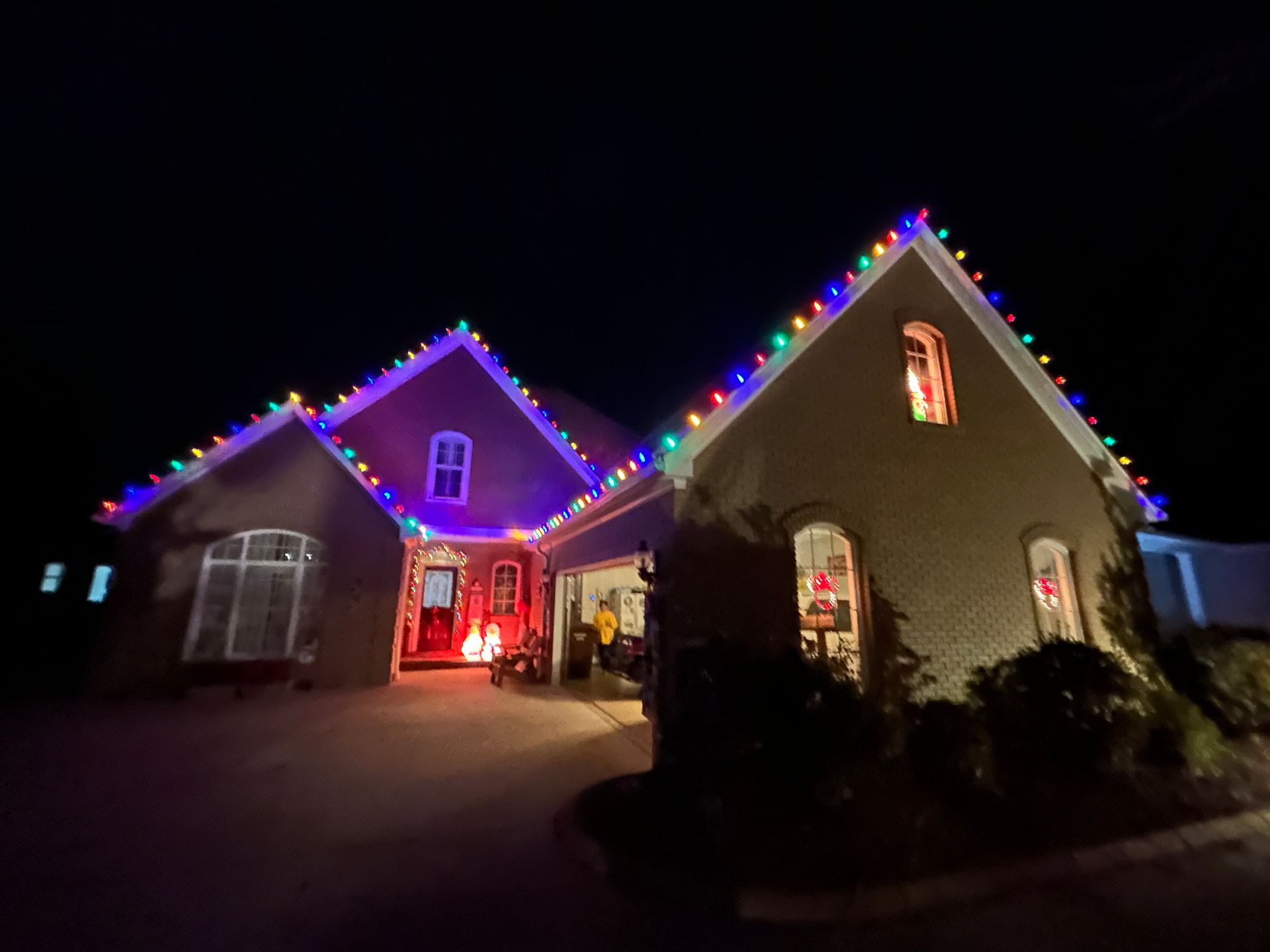 House lit with colorful Christmas lights at night, with a bright red-lit front entrance.