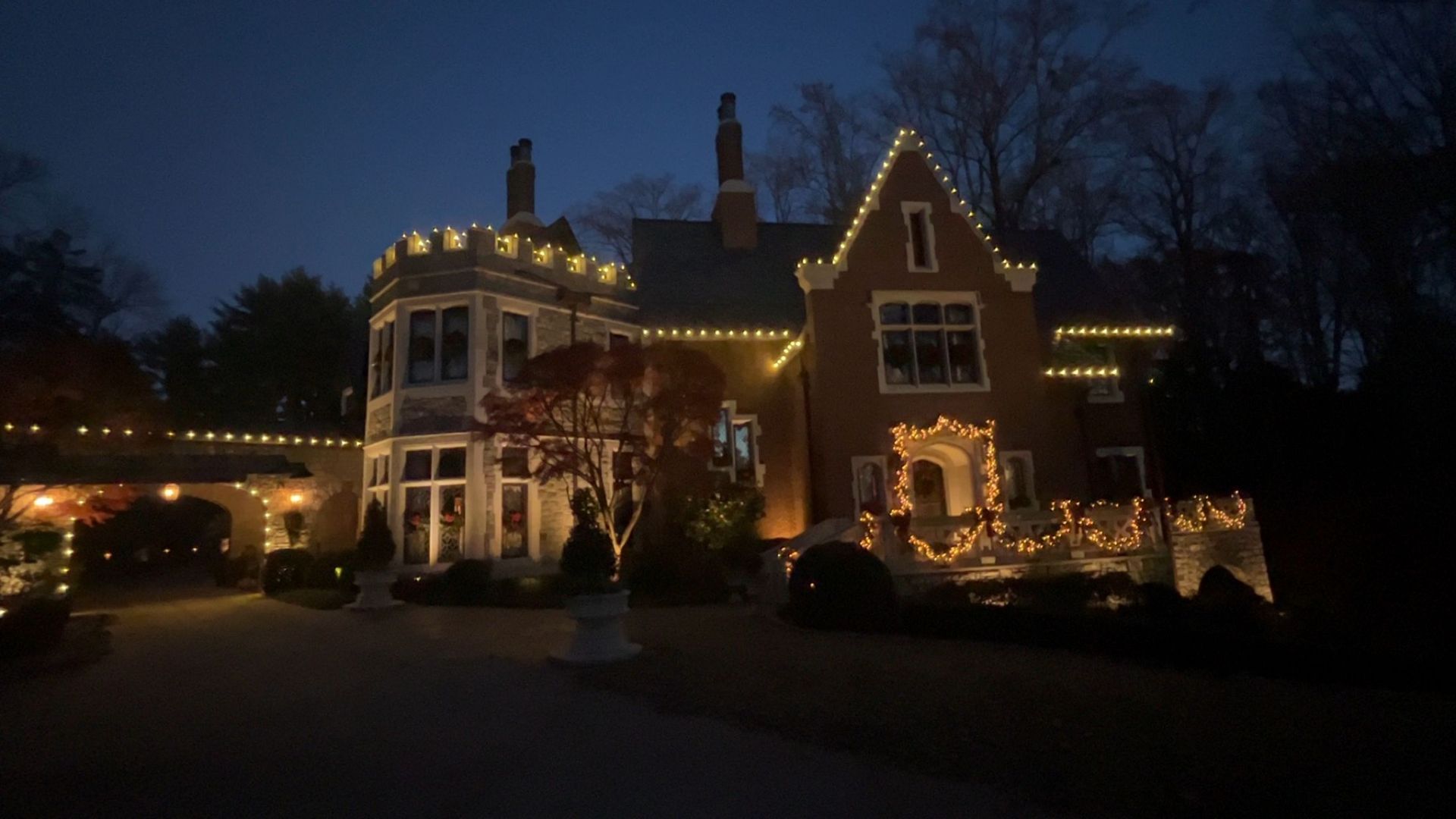 Lit house at dusk with warm holiday lights, illuminated windows, and a dark winter sky