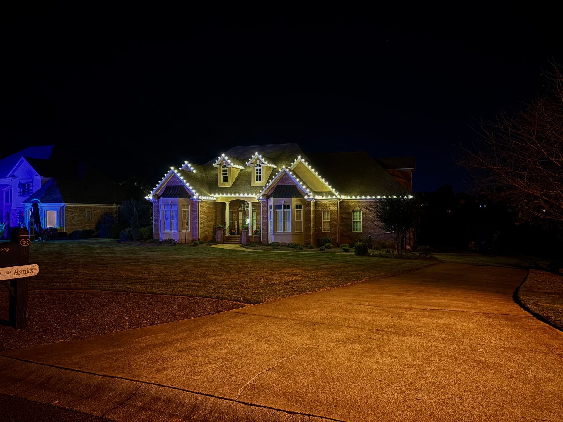Nighttime suburban house with warm holiday lights and a lit driveway