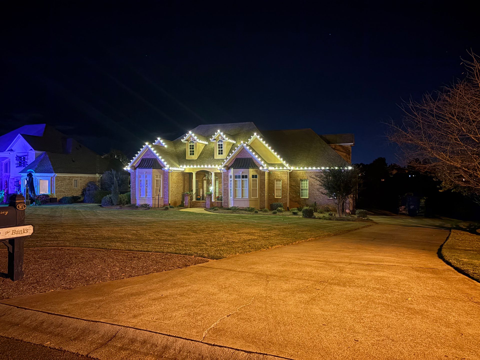 Well-lit suburban house at night with festive roof lights and a wide driveway