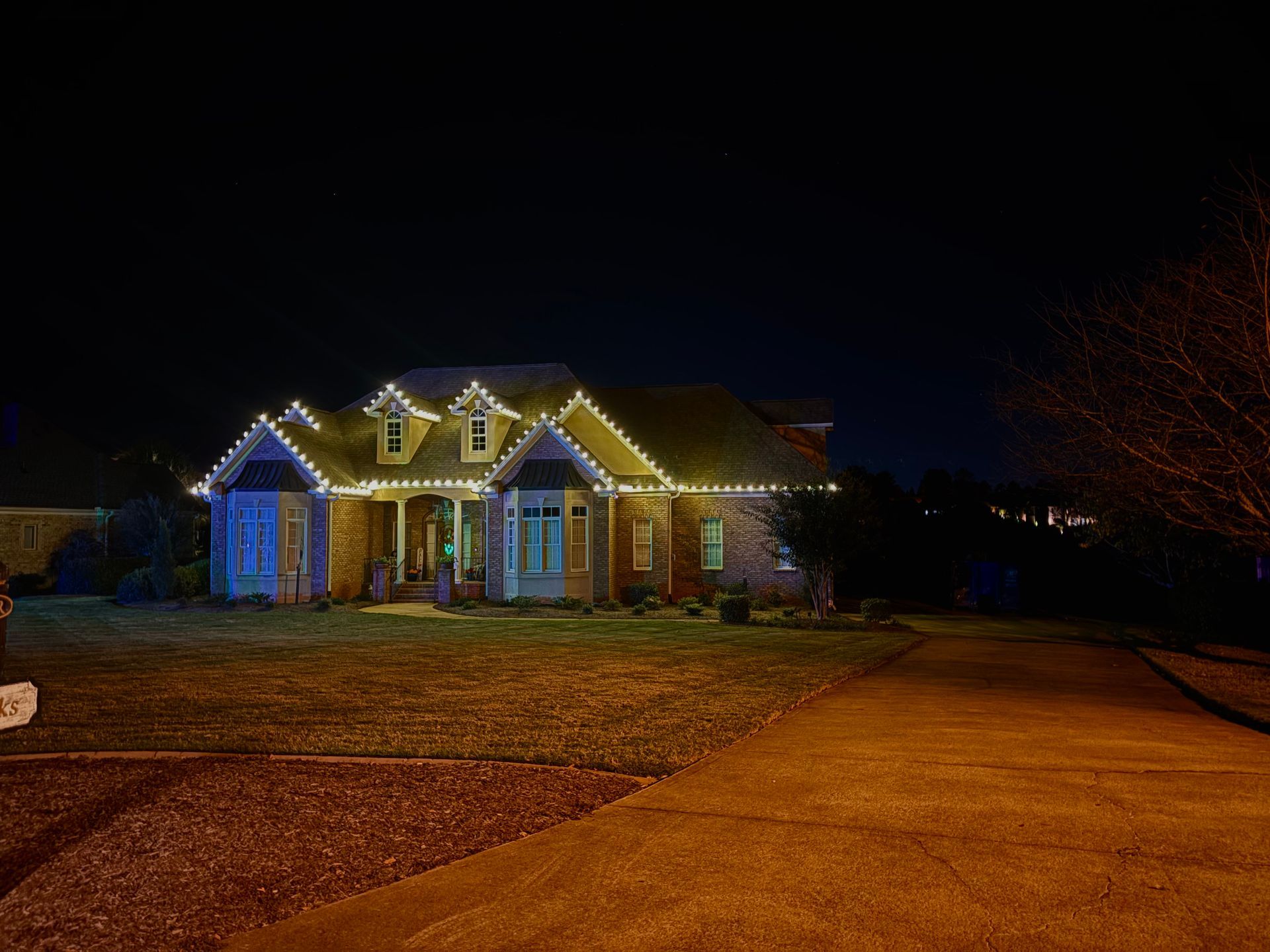 House at night with Christmas lights, lit front porch, and a driveway in the foreground