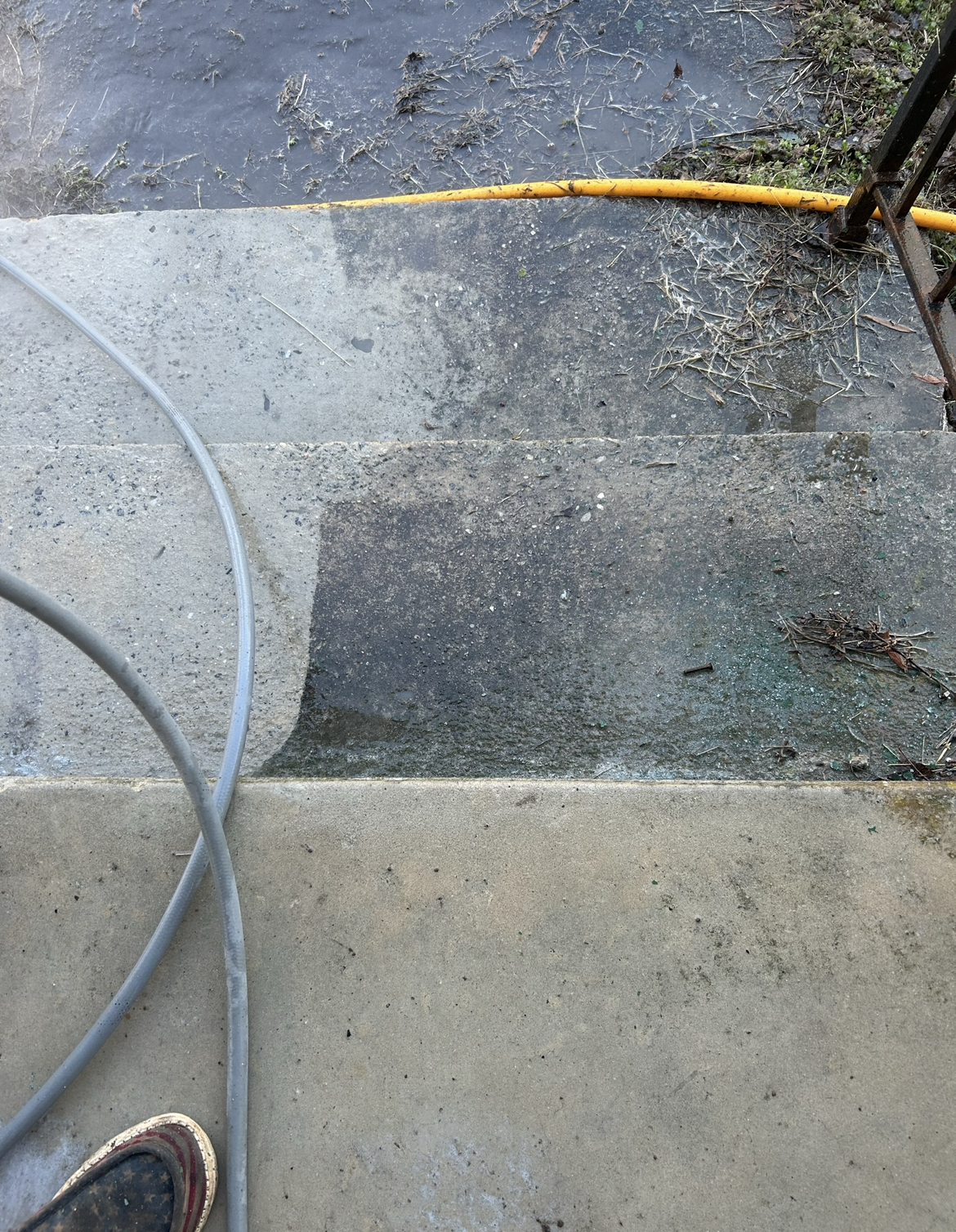 Concrete steps being pressure washed; half clean, half dirty, hose visible.