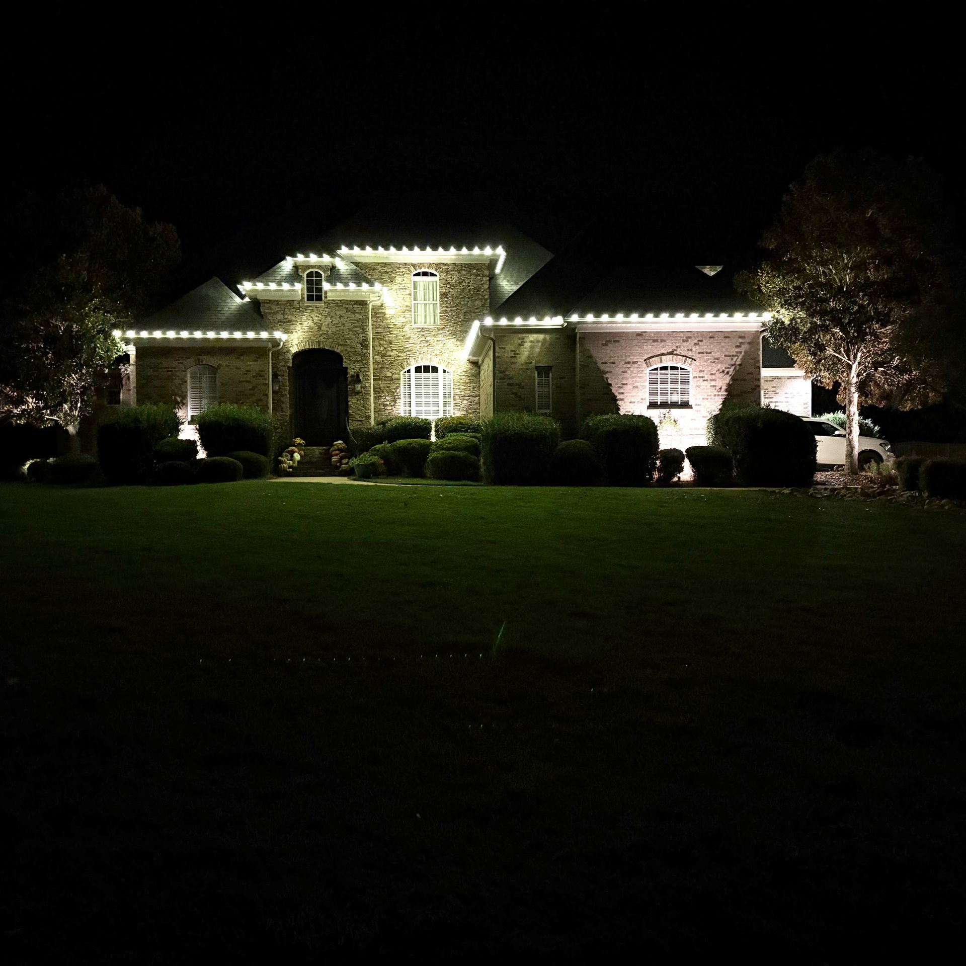 Illuminated brick house at night with white holiday lights and a lit staircase