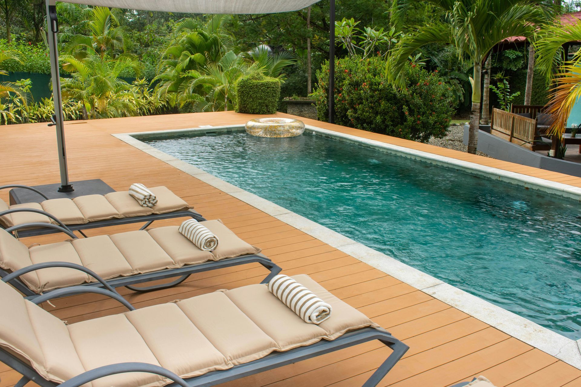 Poolside lounge chairs beside a turquoise swimming pool with tropical greenery in the background