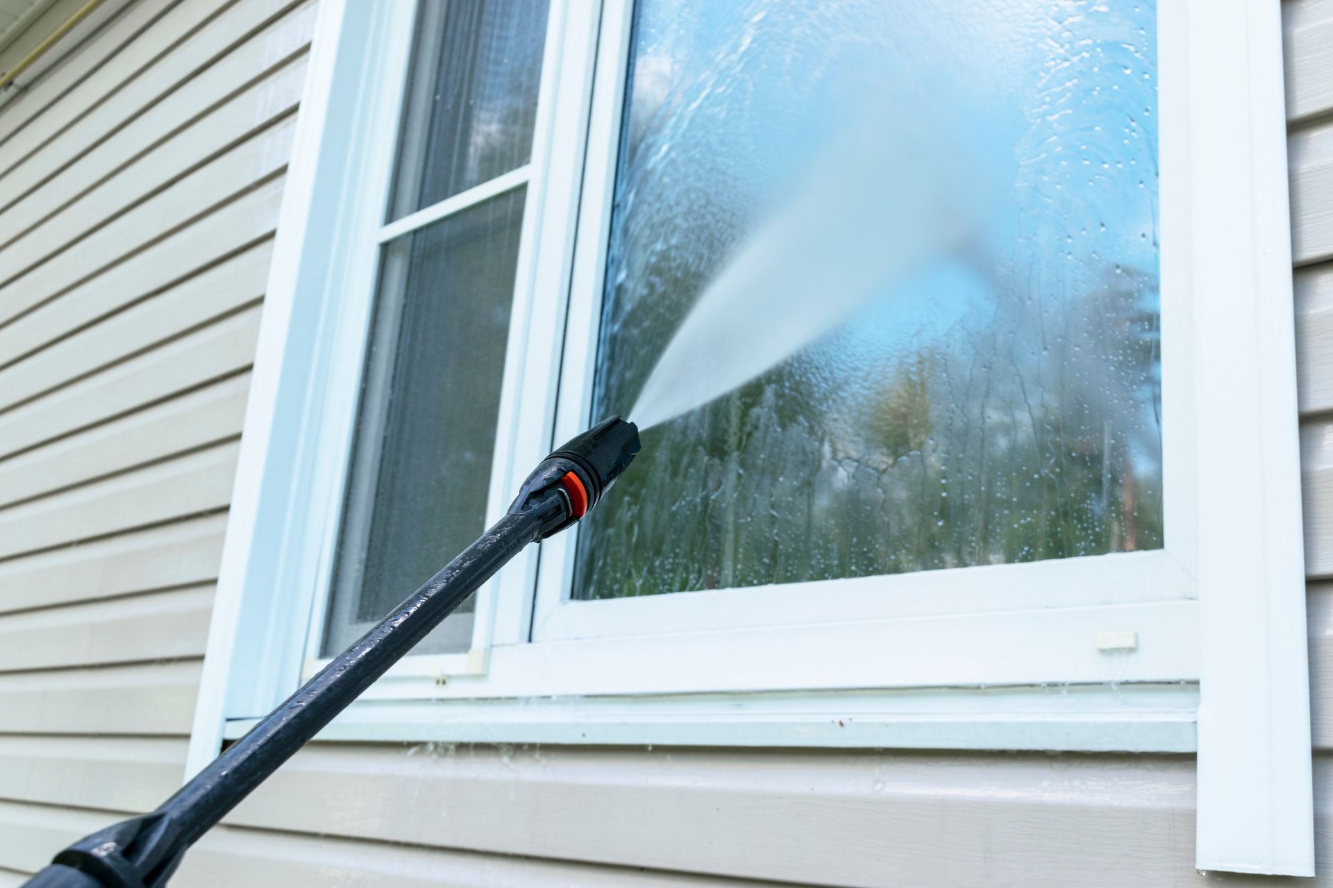 Pressure washer spraying a white house window and siding