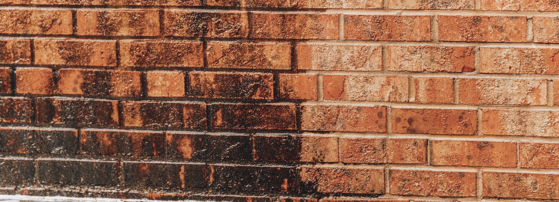 A brick wall, half cleaned, showing a contrast between dirty, dark bricks and clean, red bricks.