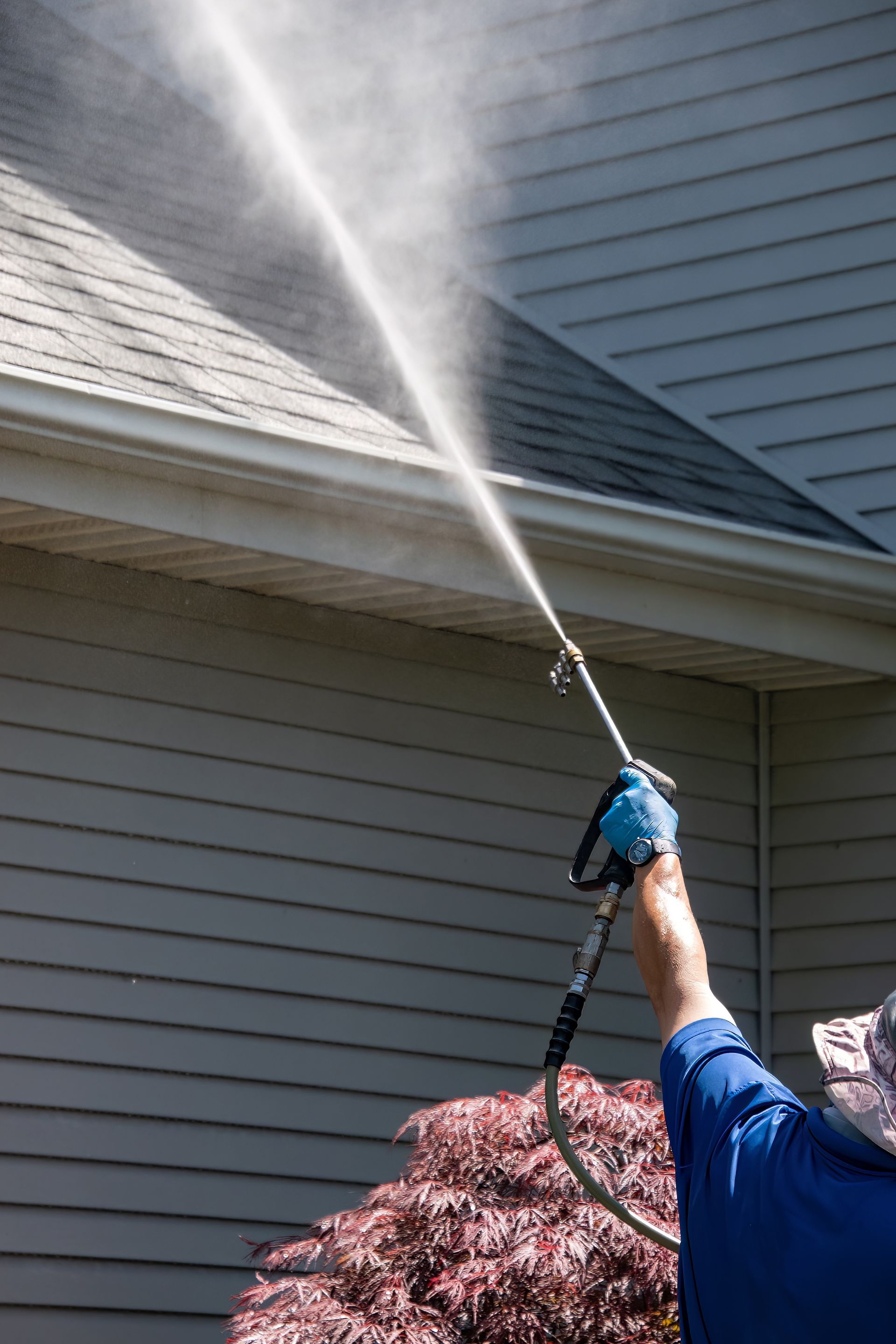Person power washing a house with a pressure washer.